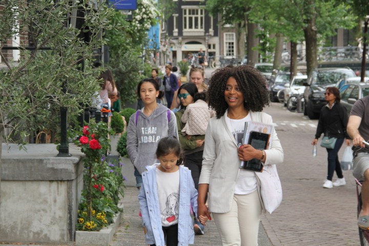 Debora is holding the hand of a kid whilst walking on a tour through Amsterdam